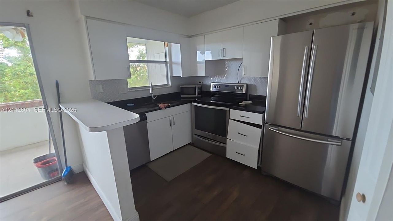Kitchen featuring white cabinetry, dark countertops, wood-finish flooring, stainless steel appliances, and an integrated breakfast bar
