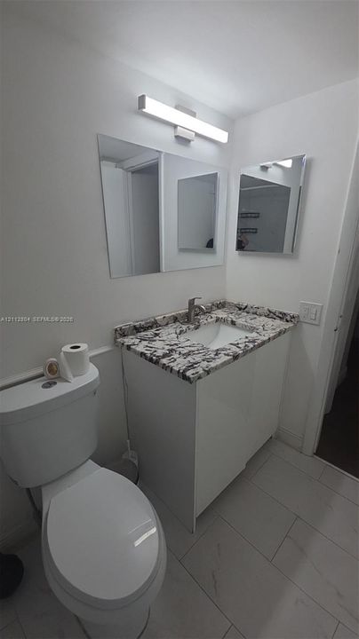 Vanity featuring a stone-patterned countertop, integrated basin, white cabinetry, wall-mounted rectangular vanity mirror, and linear LED lighting