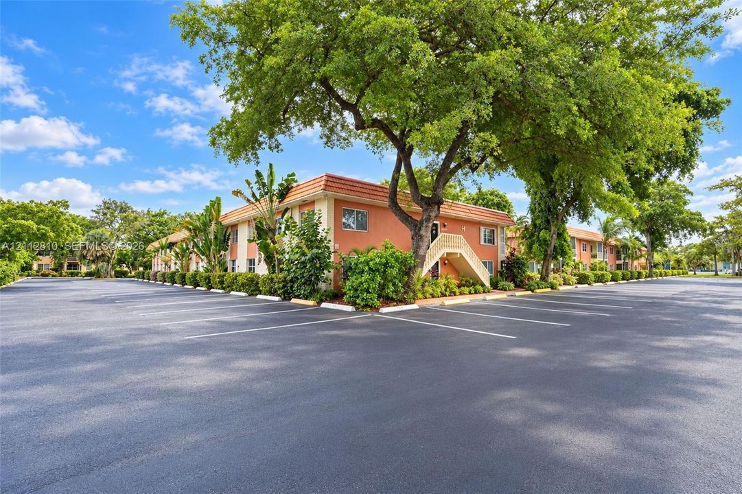 Multi-story building featuring stucco exterior walls, a tile roof, paved parking area, and mature landscaping