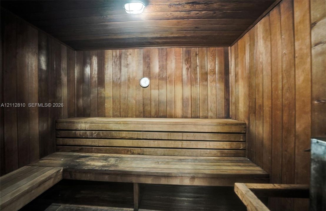 Sauna featuring cedar paneling, multi-level wooden bench seating, and overhead lighting