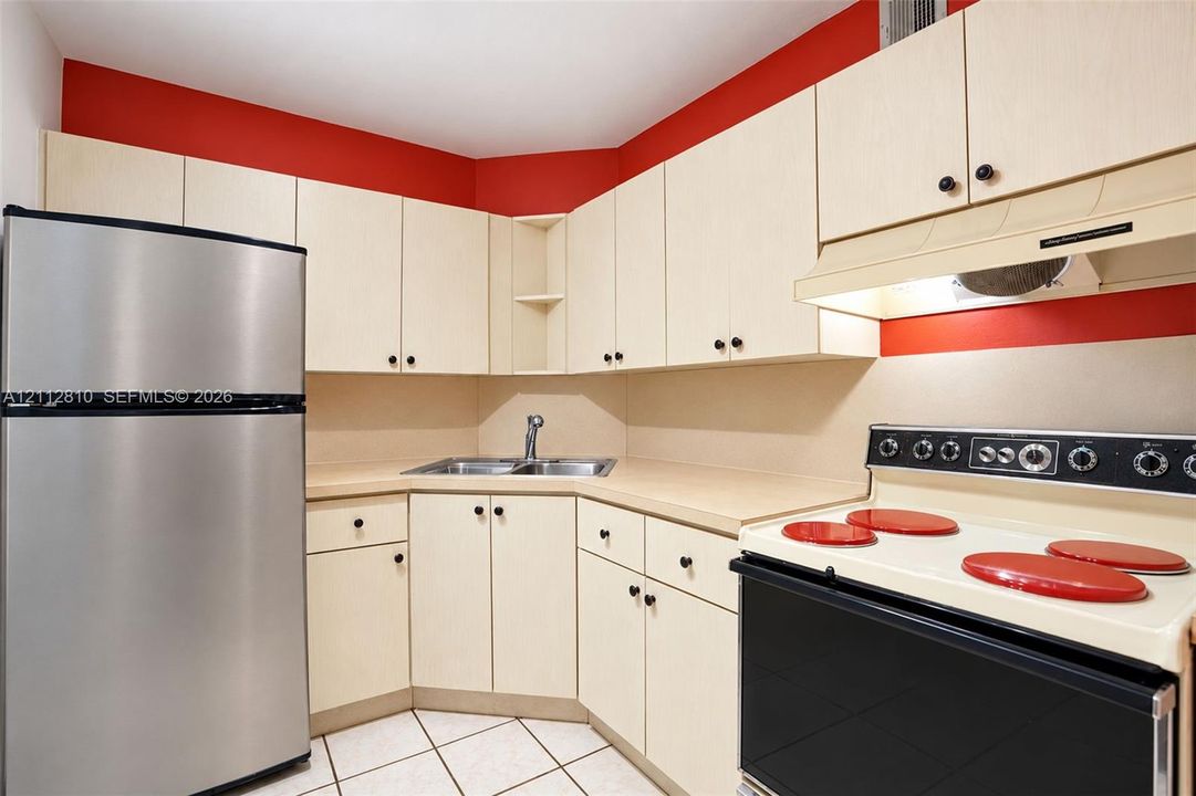 Kitchen featuring light-finish cabinetry, stainless steel refrigerator, integrated range, dual-basin sink, and tile flooring