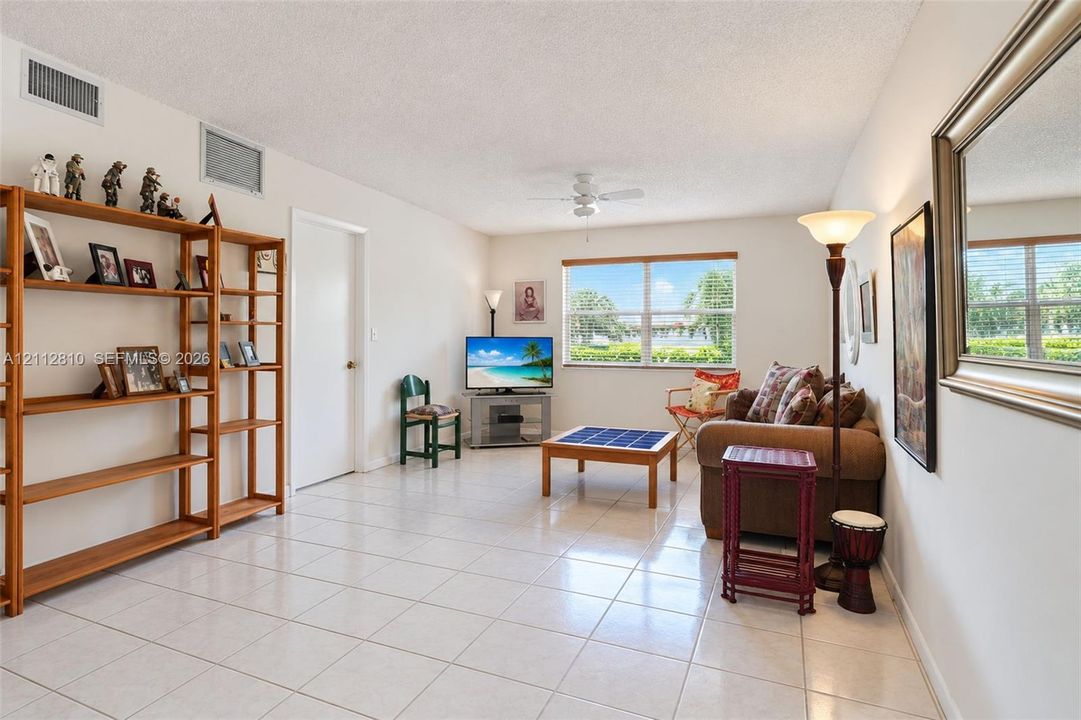 Living area featuring neutral tile flooring, a ceiling fan with integrated lighting, and a window with exterior scenery