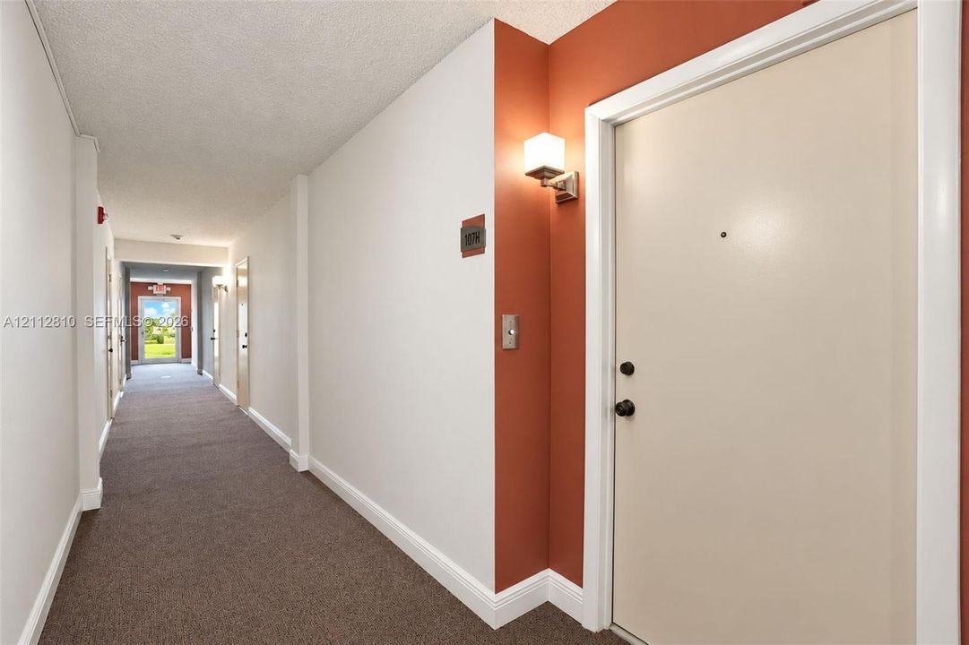 Interior hallway featuring carpeting, accent wall paint, and wall-mounted lighting fixtures