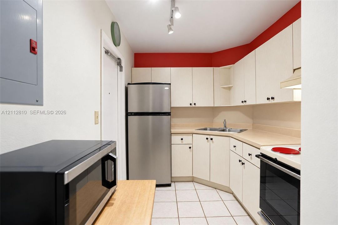 Kitchen featuring stainless steel refrigerator, white cabinetry with integrated hardware, dual-basin sink, and tile flooring