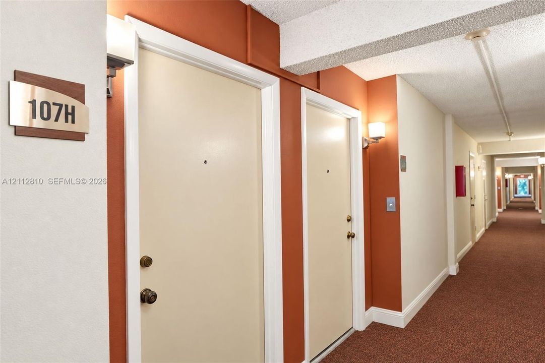 Interior hallway featuring wall-mounted light fixtures, carpeted flooring, and neutral-toned doors with metallic hardware
