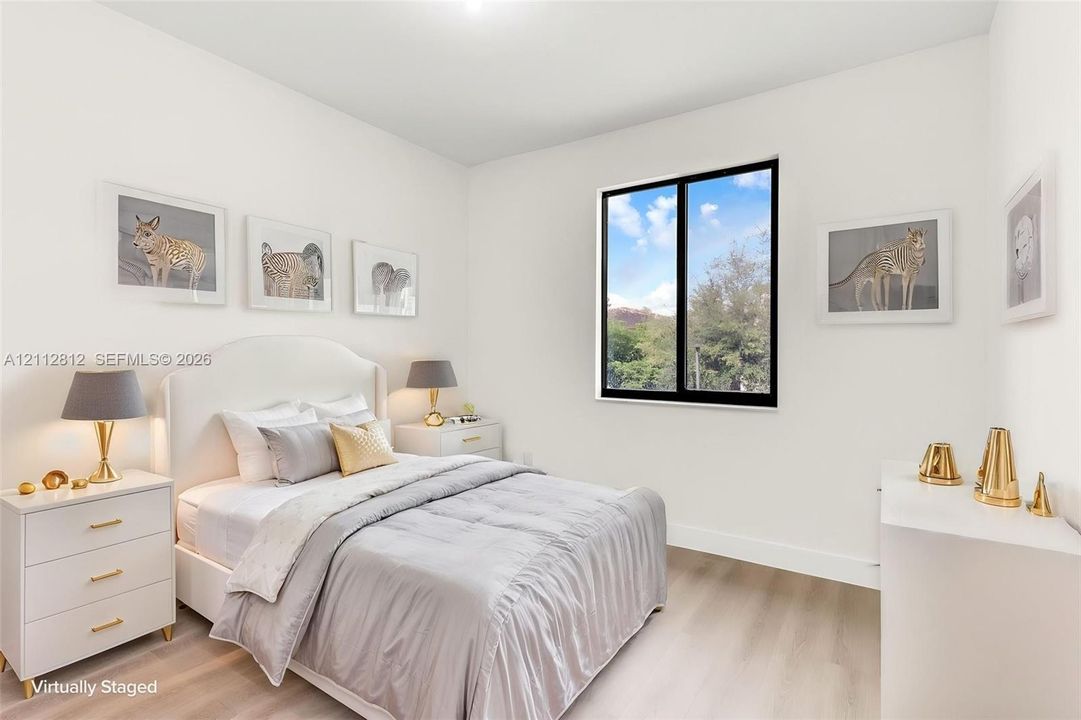 Neutral-toned interior space featuring light wood-finish flooring, crisp white walls, and a large black-framed window