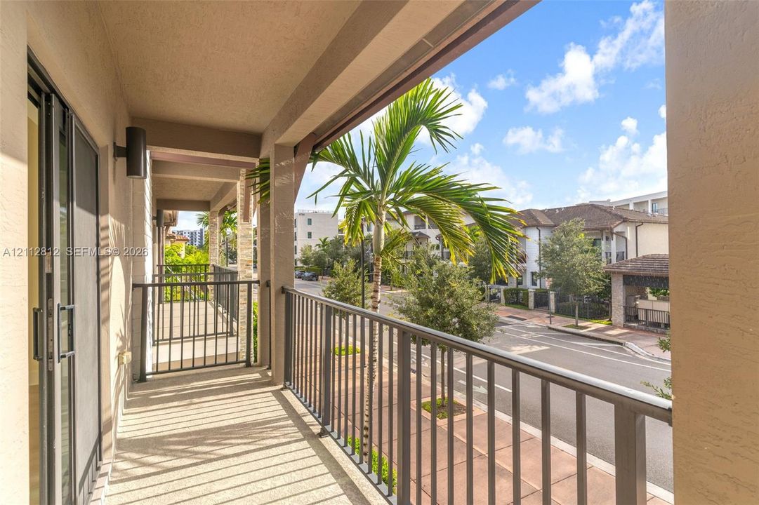 Covered balcony featuring textured concrete flooring, metal railings, and wall-mounted exterior lighting