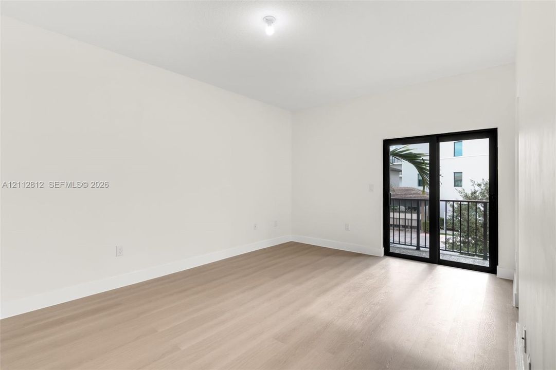 Interior space featuring neutral wall tones, wood-finish flooring, and black-framed sliding glass doors opening to a balcony with metal railing