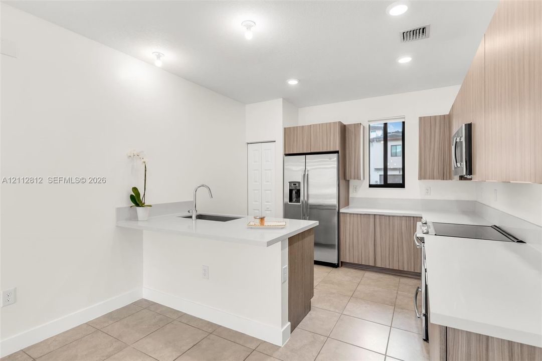 Kitchen featuring wood-finish cabinetry, solid surface countertops, stainless steel appliances, and ceramic tile flooring