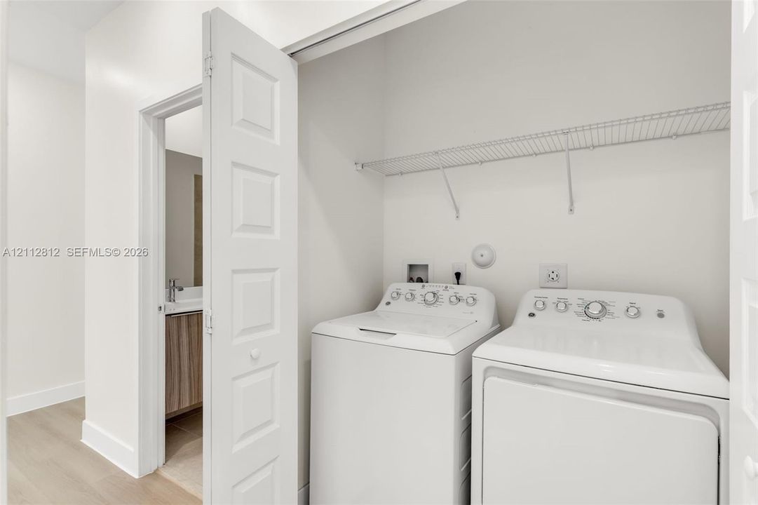 Laundry closet featuring wire shelving and a white washer and dryer set, with interior door access to a bathroom vanity
