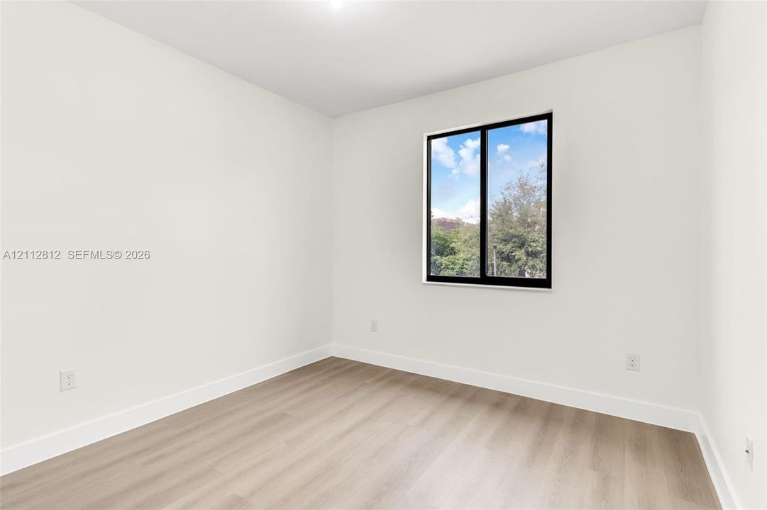 Neutral-toned room featuring light wood-finish flooring, crisp white walls, and a single-pane black-framed window