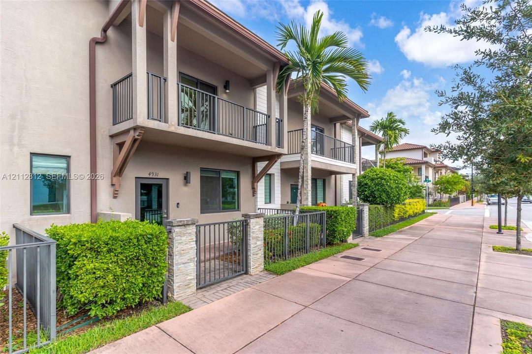 Two-story exterior featuring a private upper-level balcony, stacked-stone entry columns, metal fencing, and landscaped shrubbery