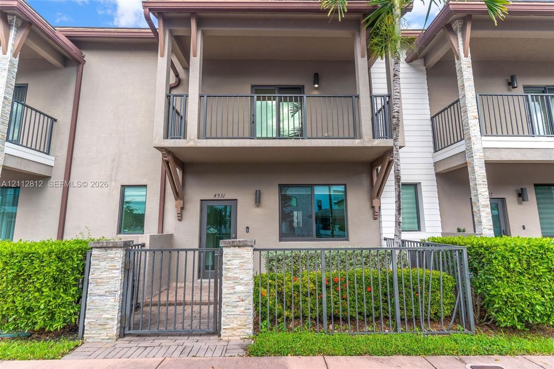 Exterior facade featuring stucco siding, stone-accented masonry pillars, a private fenced courtyard, and an upper-level covered balcony with metal railings