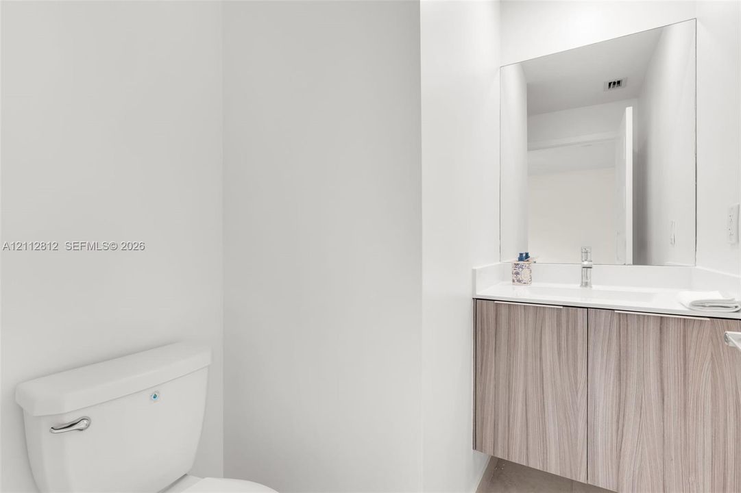 Floating wood-finish vanity with a white countertop, integrated sink, chrome faucet, and expansive wall-mounted mirror