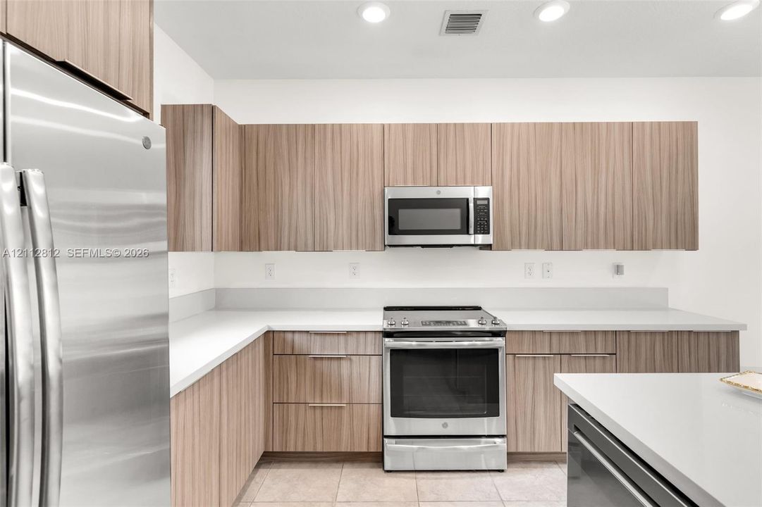 Kitchen featuring wood-finish cabinetry, solid surface countertops, stainless steel appliances, built-in microwave, and recessed lighting