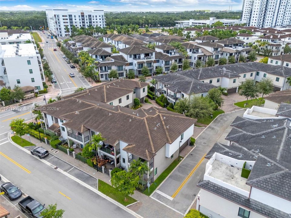 Aerial perspective featuring multi-story residential architecture with shingled rooflines, exterior balconies, paved surface access, and landscaping including mature trees and shrubs