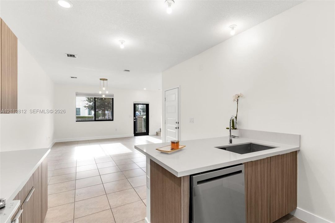 Kitchen featuring light-tone cabinetry, stone-surface countertops, an undermount sink, a stainless steel dishwasher, and tile flooring