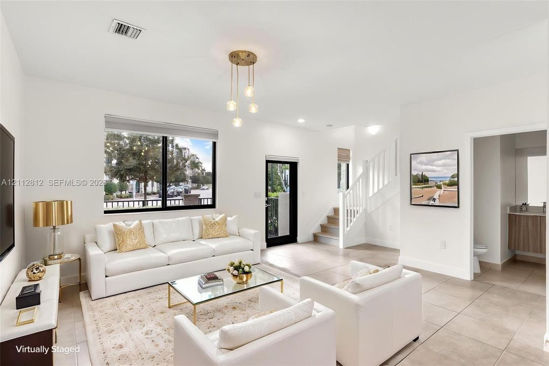 Open-concept interior featuring large-format ceramic tile flooring, multi-globe pendant lighting, a glass-panel exterior door, and a staircase with white balusters