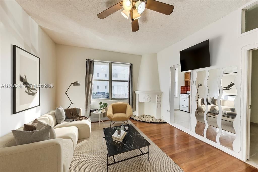 Living space featuring wood-finish flooring, a decorative fireplace with a stone-accented hearth, and a floor-to-ceiling mirrored wall