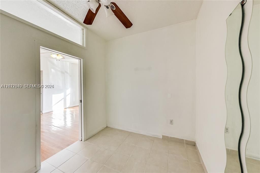Room featuring light-toned tile flooring, a ceiling fan with wood-finish blades, and a rectangular transom window positioned above a doorway