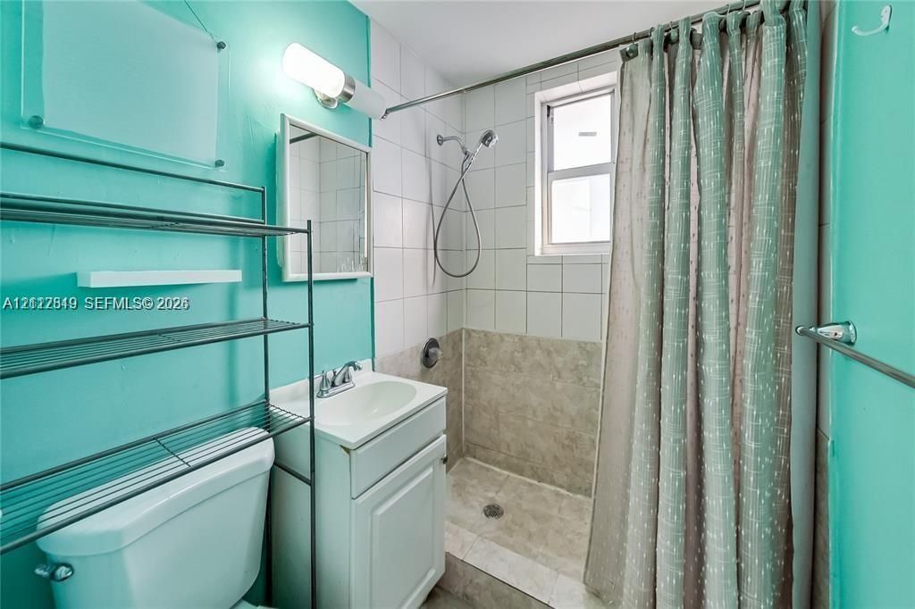 Bathroom featuring a vanity with an integrated sink, wall-mounted light fixture, shower enclosure with tile surround, and a window