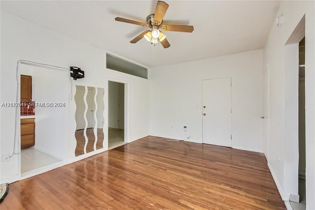 Living area featuring wood-finish flooring, a ceiling fan with integrated lighting, and a transom window
