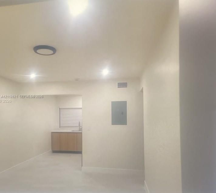 Interior space featuring neutral wall paint, recessed lighting, surface-mounted circular ceiling fixture, and kitchen area with light-toned wooden cabinetry