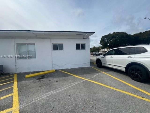 Exterior structure with white stucco finish, asphalt parking surface, and painted yellow parking stalls