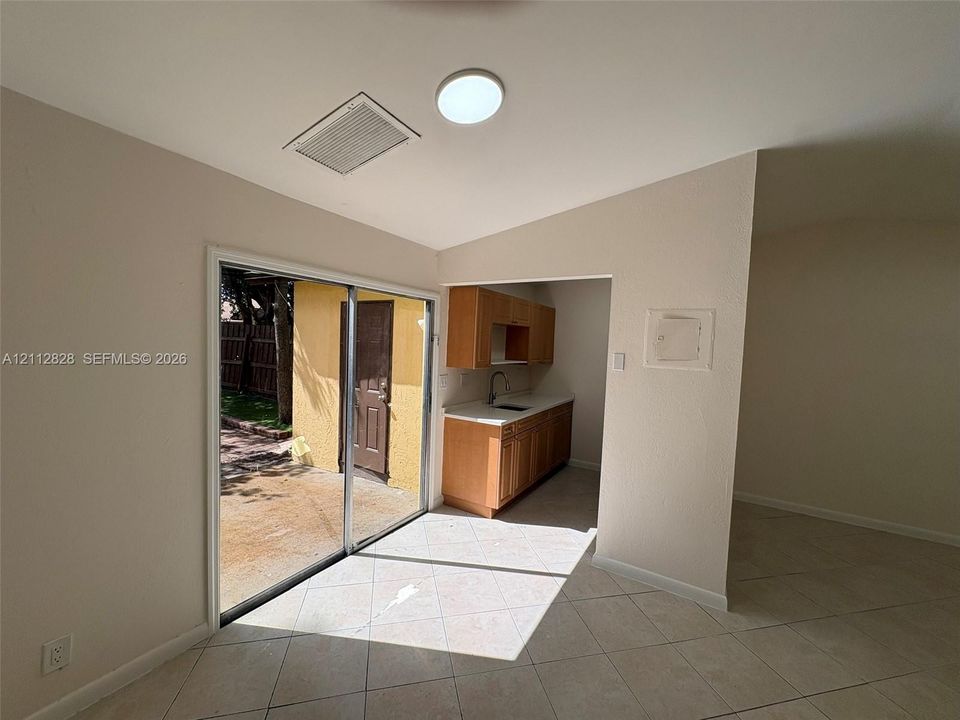 Sliding glass door, light-colored tile flooring, wood-finish cabinetry, countertop with a drop-in sink, and vaulted ceiling