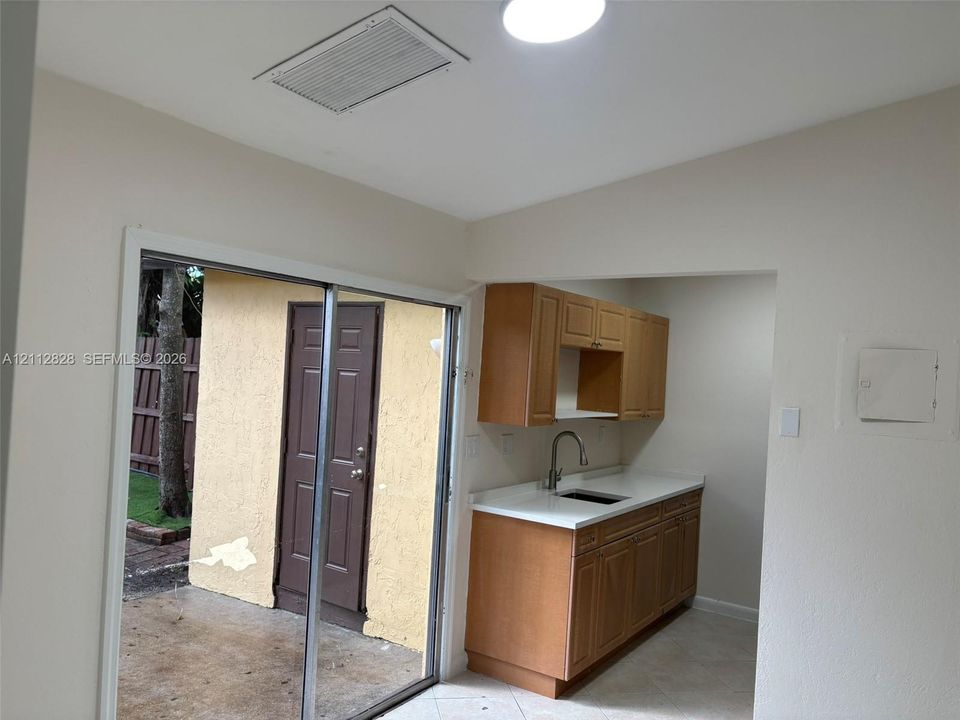 Kitchen featuring wood cabinetry, white countertops, and a stainless steel sink with a gooseneck faucet, accompanied by sliding glass doors opening to an exterior patio with a textured wall finish
