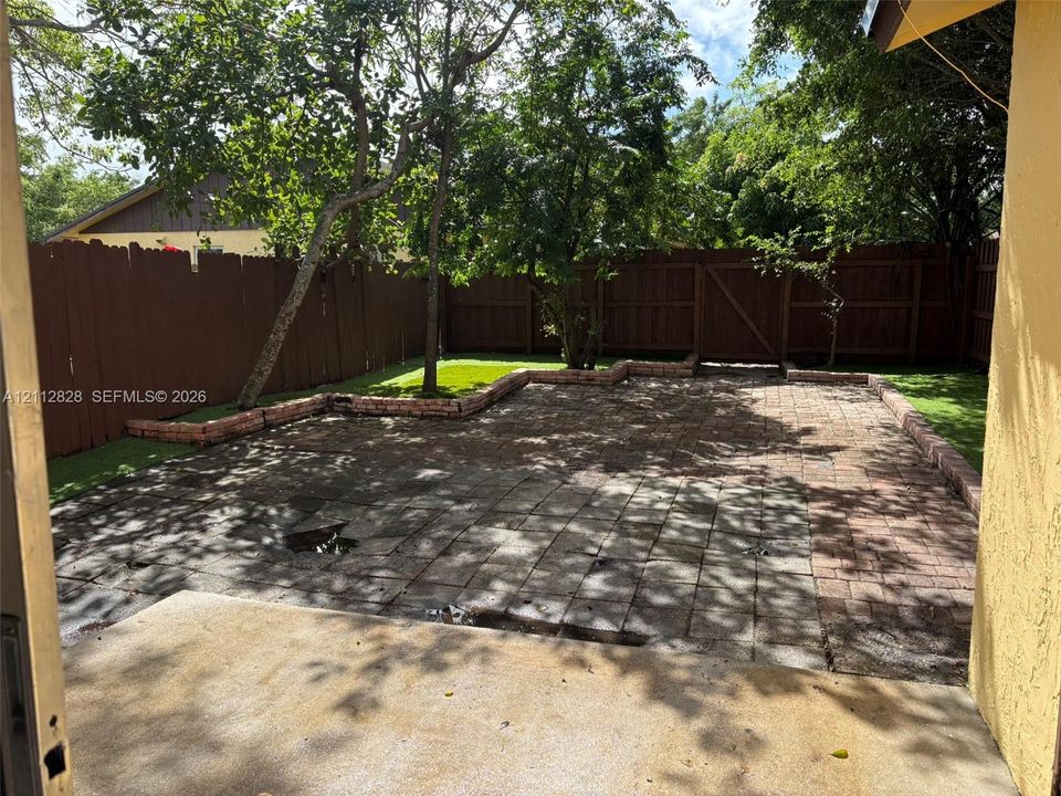 Backyard featuring a paved brick patio, raised masonry garden edging, and a wood privacy fence