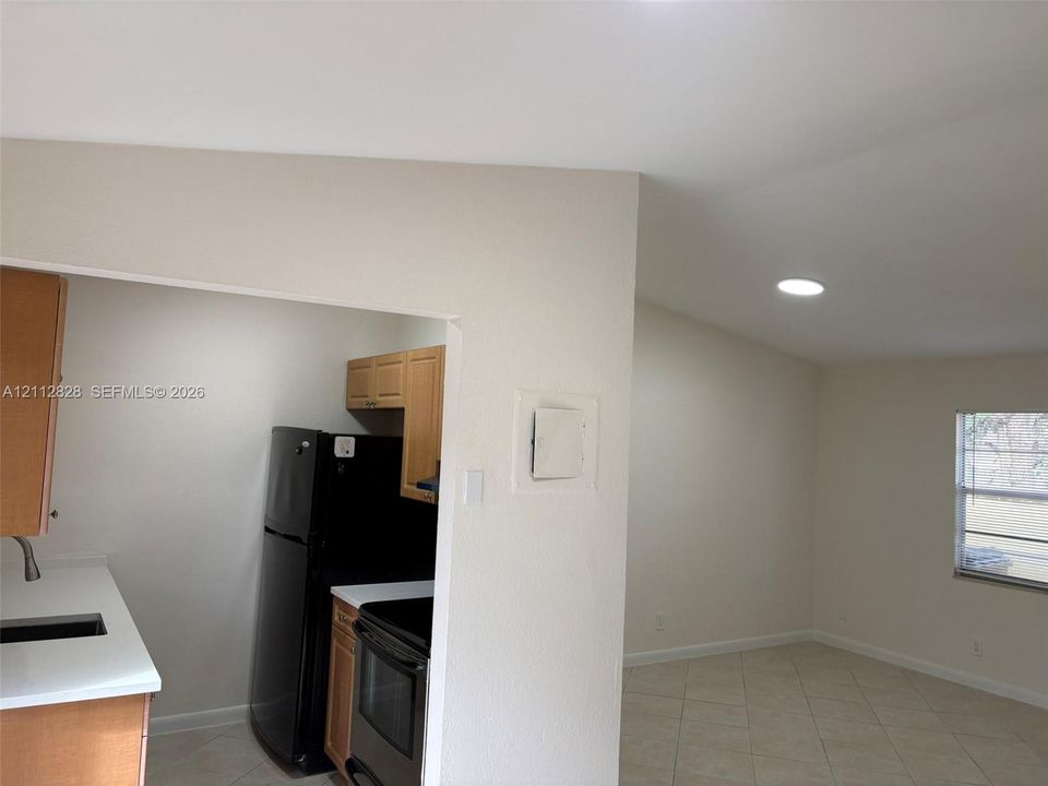 Kitchen featuring wood cabinetry, solid-surface countertops, and black appliances, paired with a room finished with tile flooring and recessed lighting