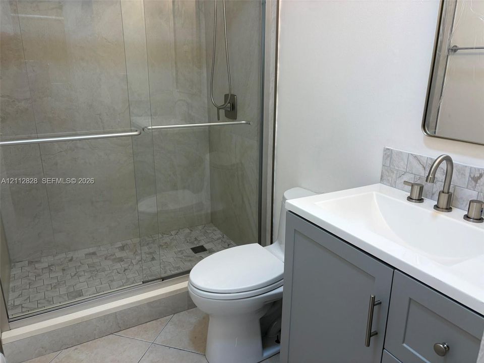 Bathroom featuring a walk-in shower with sliding glass doors, a vanity with a white countertop and undermount sink, stone-finish backsplash, and a wall-mounted mirror