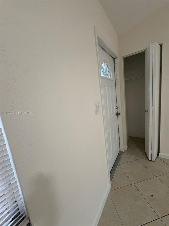 Entryway featuring tile flooring, a paneled door with an arched window inlay, and a built-in closet with folding doors