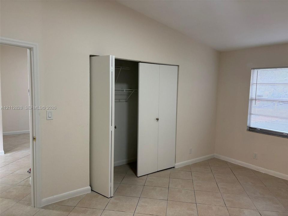 Interior room featuring neutral wall tones, large-format tile flooring, a closet with bifold doors and integrated shelving, and a window with horizontal blinds