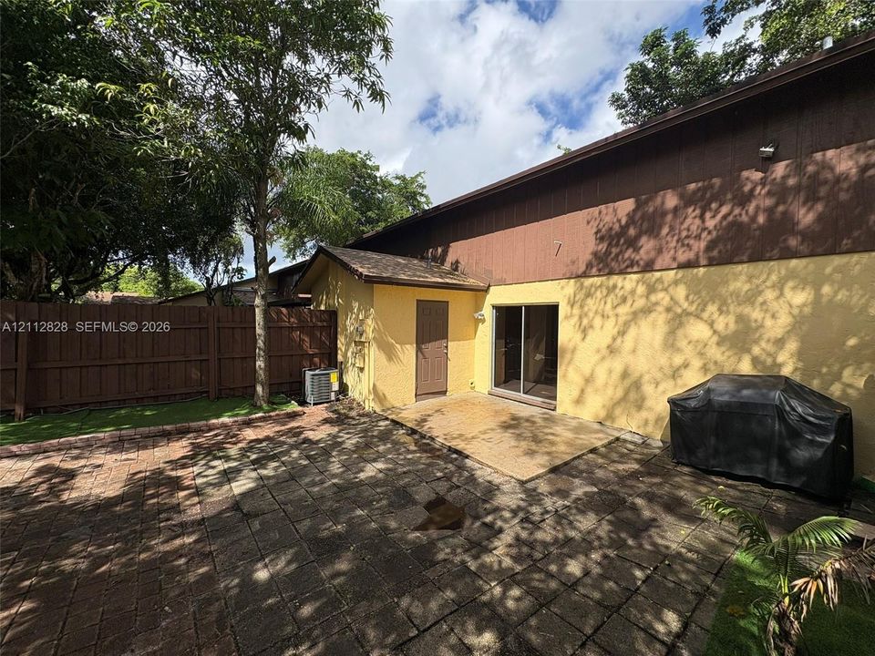 Rear exterior featuring a paved stone patio, dual-tone stucco and wood siding, a sliding glass door, and a privacy-fenced yard