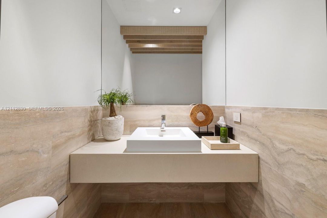 Floating vanity featuring a square vessel sink, full-width wall mirror, exposed wooden ceiling beams, and natural stone wall cladding