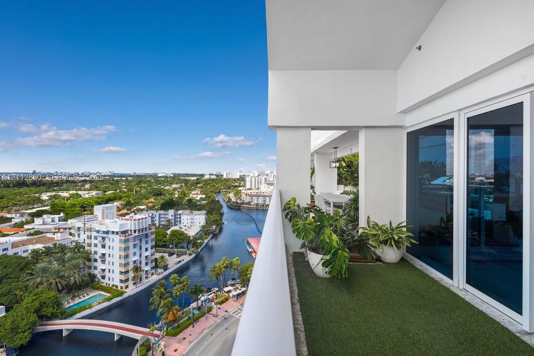 Covered outdoor balcony featuring synthetic turf surfacing, a solid white structural railing, and multi-panel floor-to-ceiling glass sliding doors