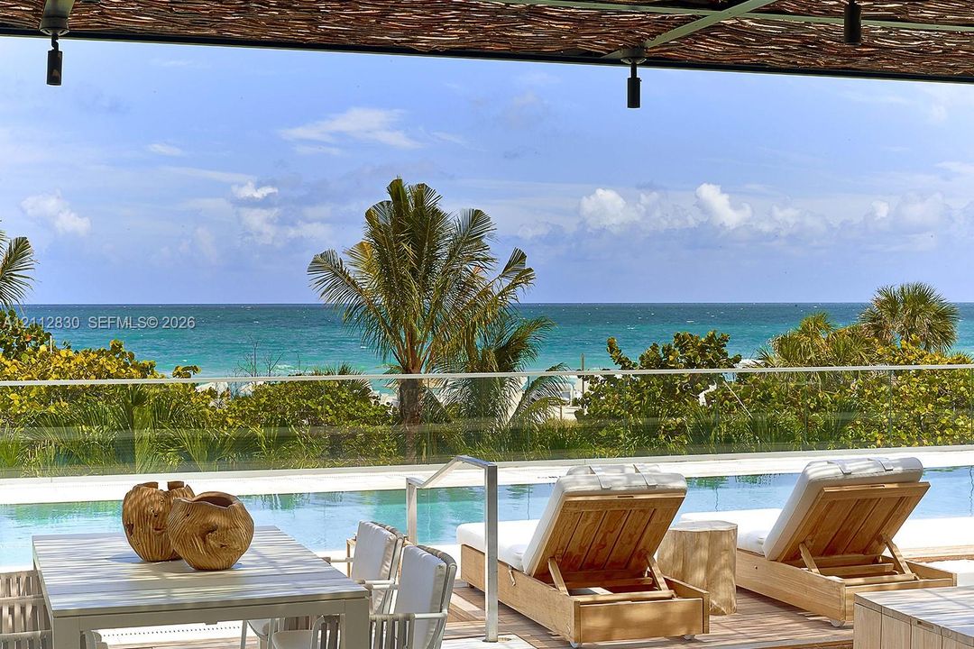 Outdoor terrace featuring a swimming pool with a glass railing and direct ocean exposure