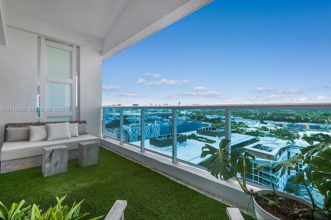 Covered balcony featuring synthetic turf flooring and a glass railing with metal framing
