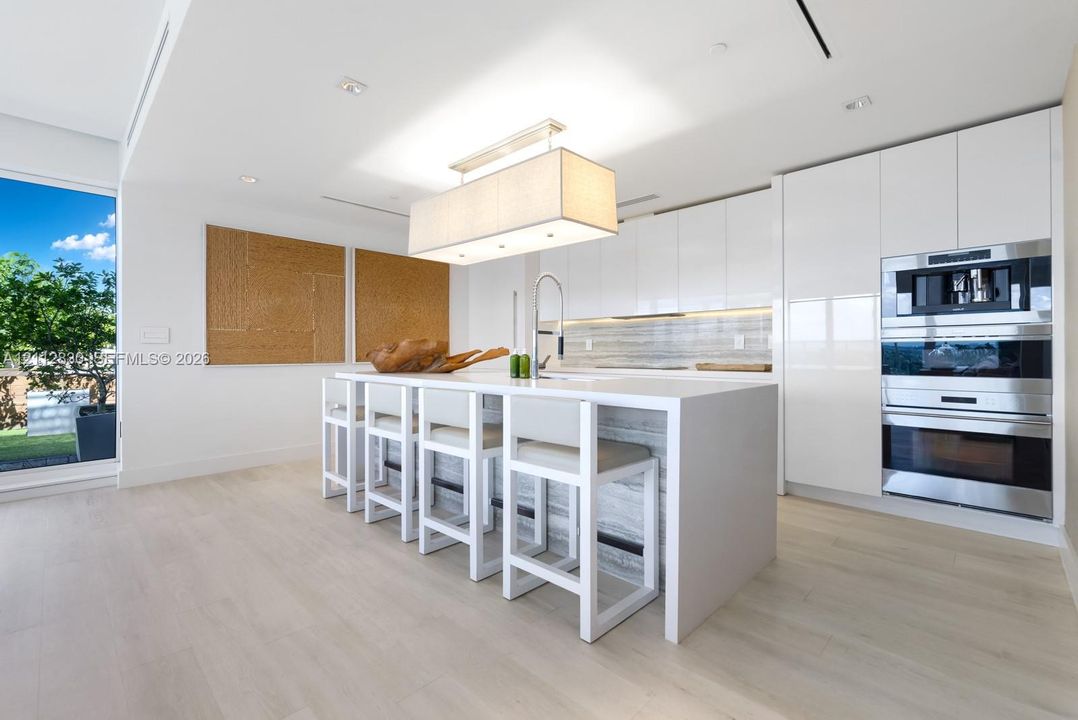 Modern kitchen featuring a waterfall-edge island, high-gloss flat-panel cabinetry, integrated stainless steel appliances, and wood-finish flooring