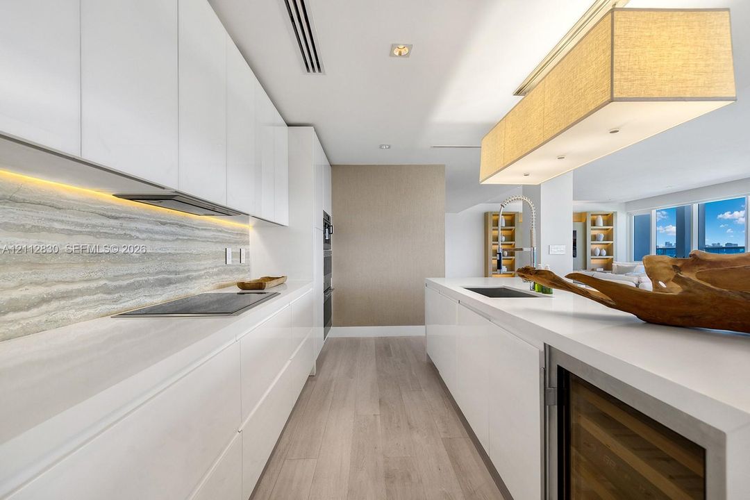 Kitchen featuring high-gloss cabinetry, stone-finish backsplash with integrated under-cabinet lighting, solid-surface countertops, wood-finish flooring, and a built-in wine cooler