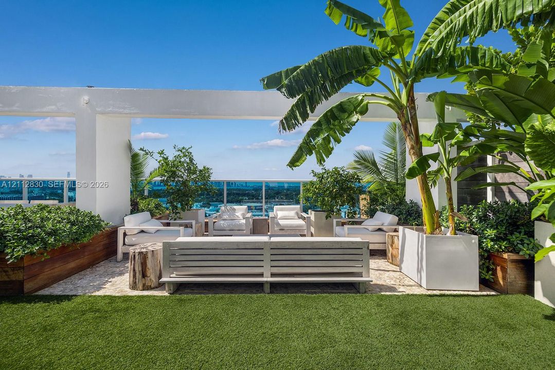 Rooftop terrace featuring artificial turf, built-in wooden planters, glass railings, and a structural pergola