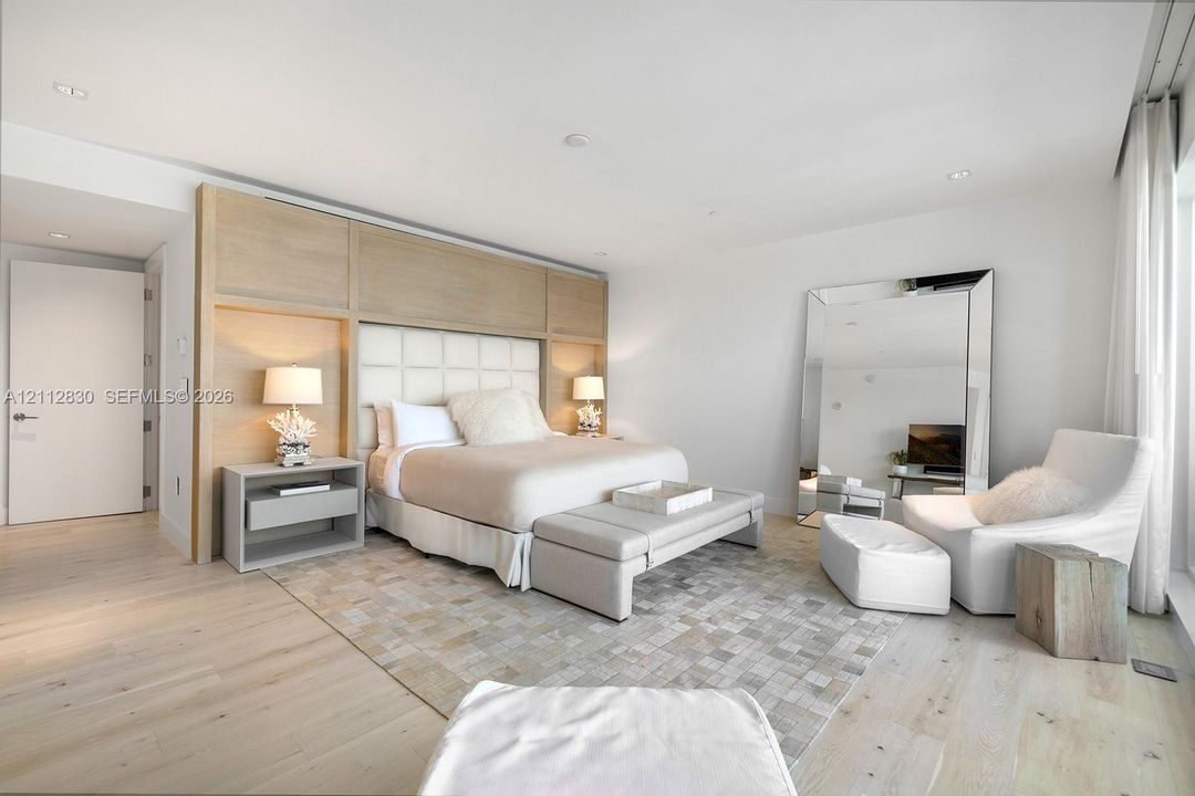Light-toned wood-finish flooring, custom built-in wood-panel headboard with integrated lighting, and recessed ceiling lighting