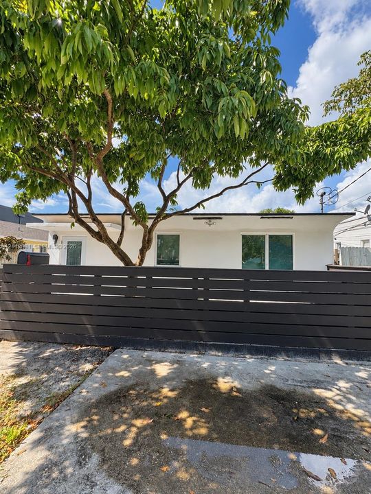 Stucco exterior featuring horizontal slat privacy fencing, dual-pane windows, and a mature shade tree