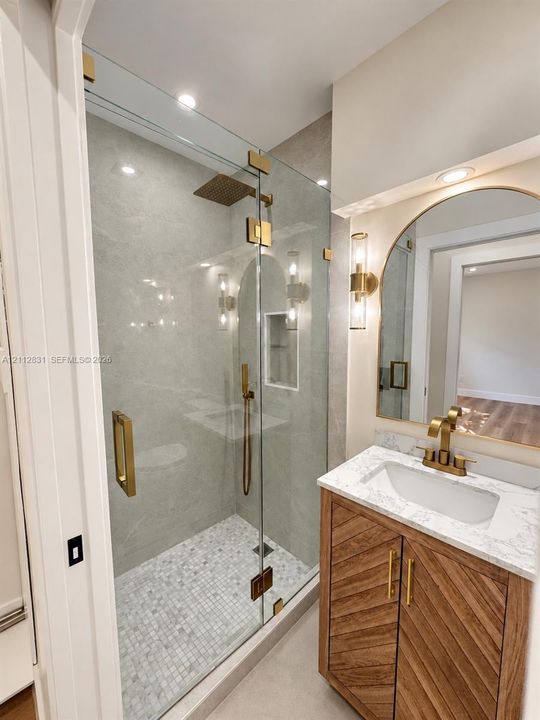 Walk-in shower featuring a glass enclosure with metallic gold-finish hardware, built-in wall niche, and mosaic tile flooring