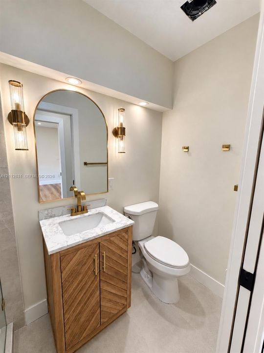 Vanity featuring a chevron-patterned wood cabinet, stone-finish countertop, arched mirror, brass-finish fixtures, and dual-sconce wall lighting