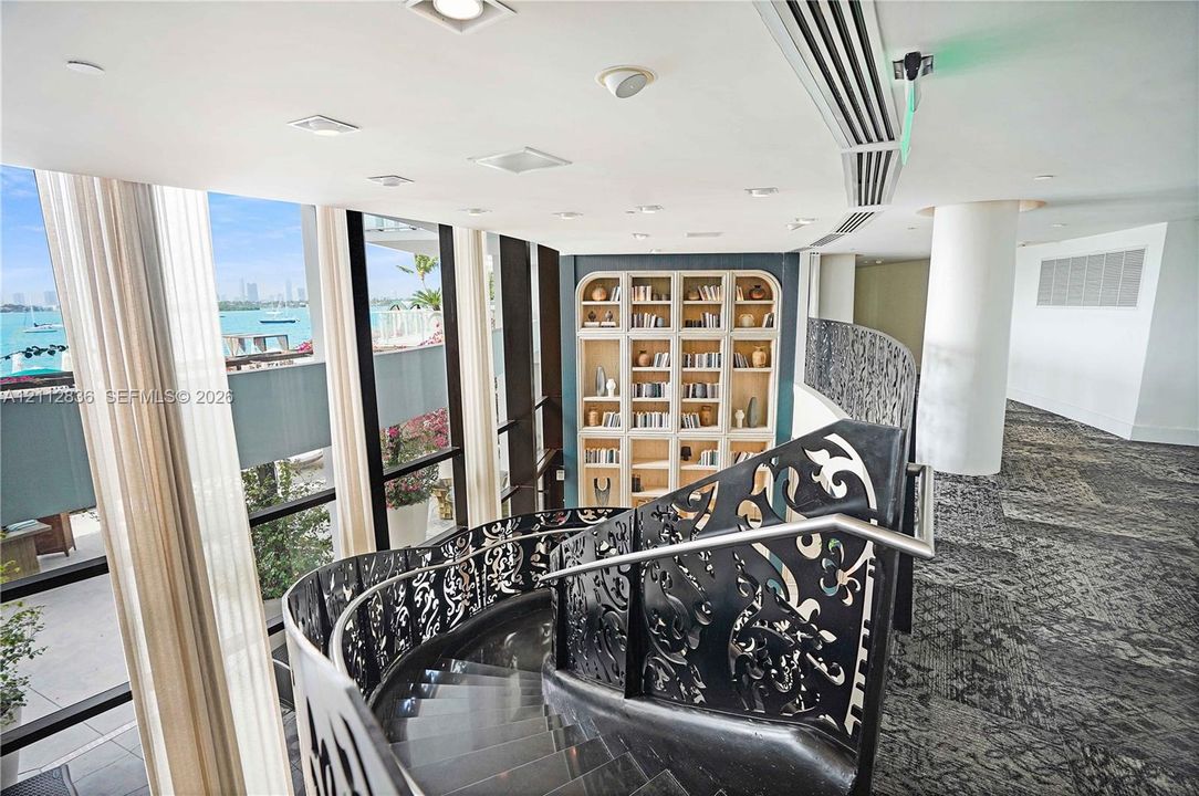 Curved staircase featuring custom laser-cut black metal railings, floor-to-ceiling glass wall panels, and a built-in recessed shelving unit