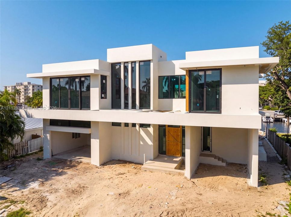 Modern two-story architectural exterior featuring smooth stucco siding, large-format glass windows, a cantilevered second-story balcony, and an integrated multi-car parking area