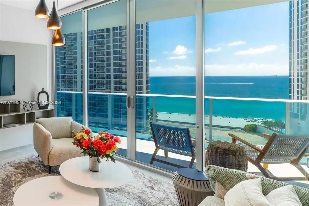 Floor-to-ceiling glass walls, expansive balcony with glass railings, built-in media shelving, and trio of pendant light fixtures